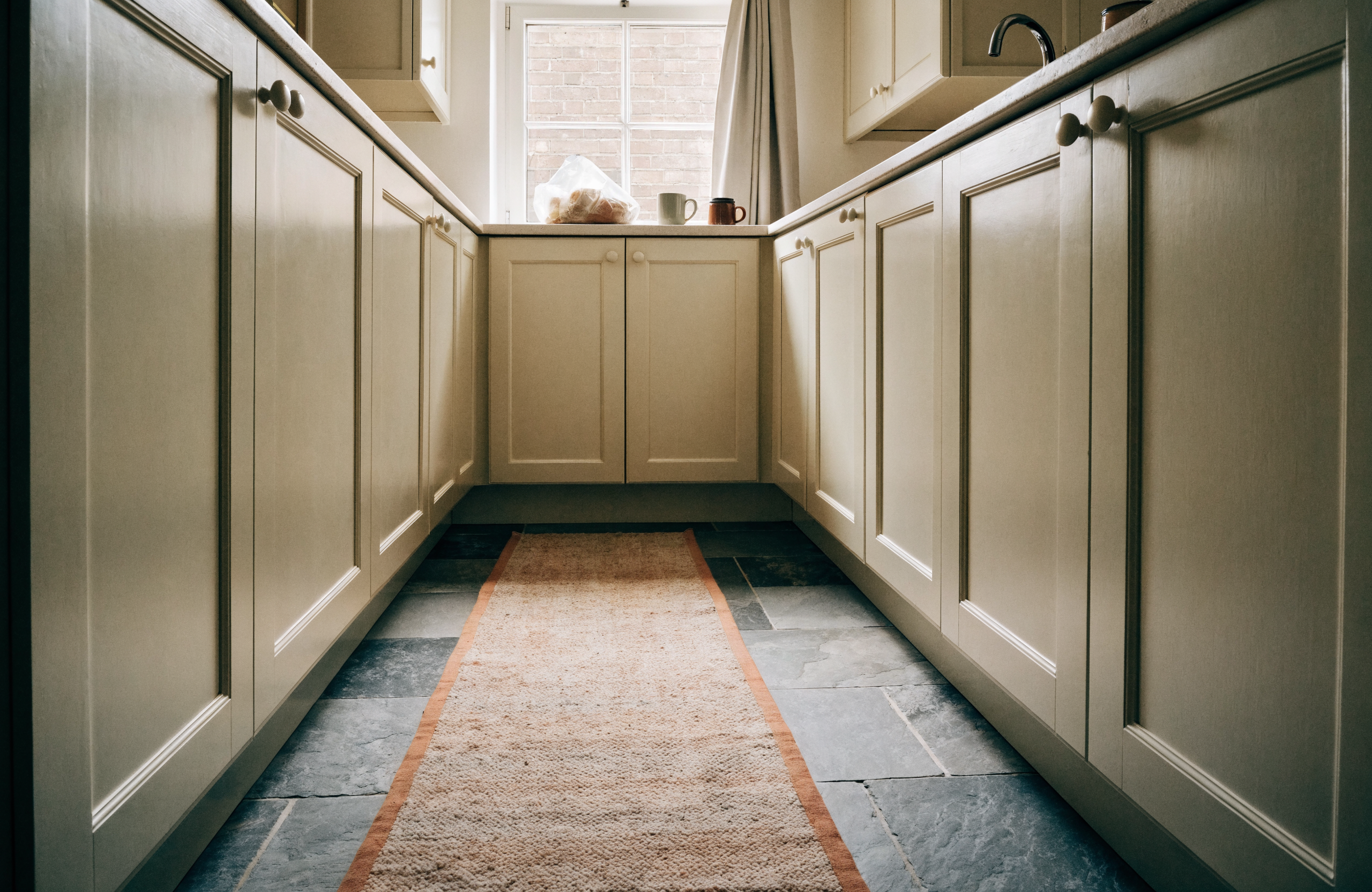 A flatweave runner laid along a galley kitchen on a slate tile floor